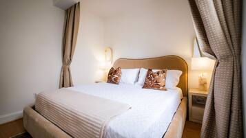 A neatly made bed with a beige blanket, two bedside lamps, and a nightstand with a tissue box.