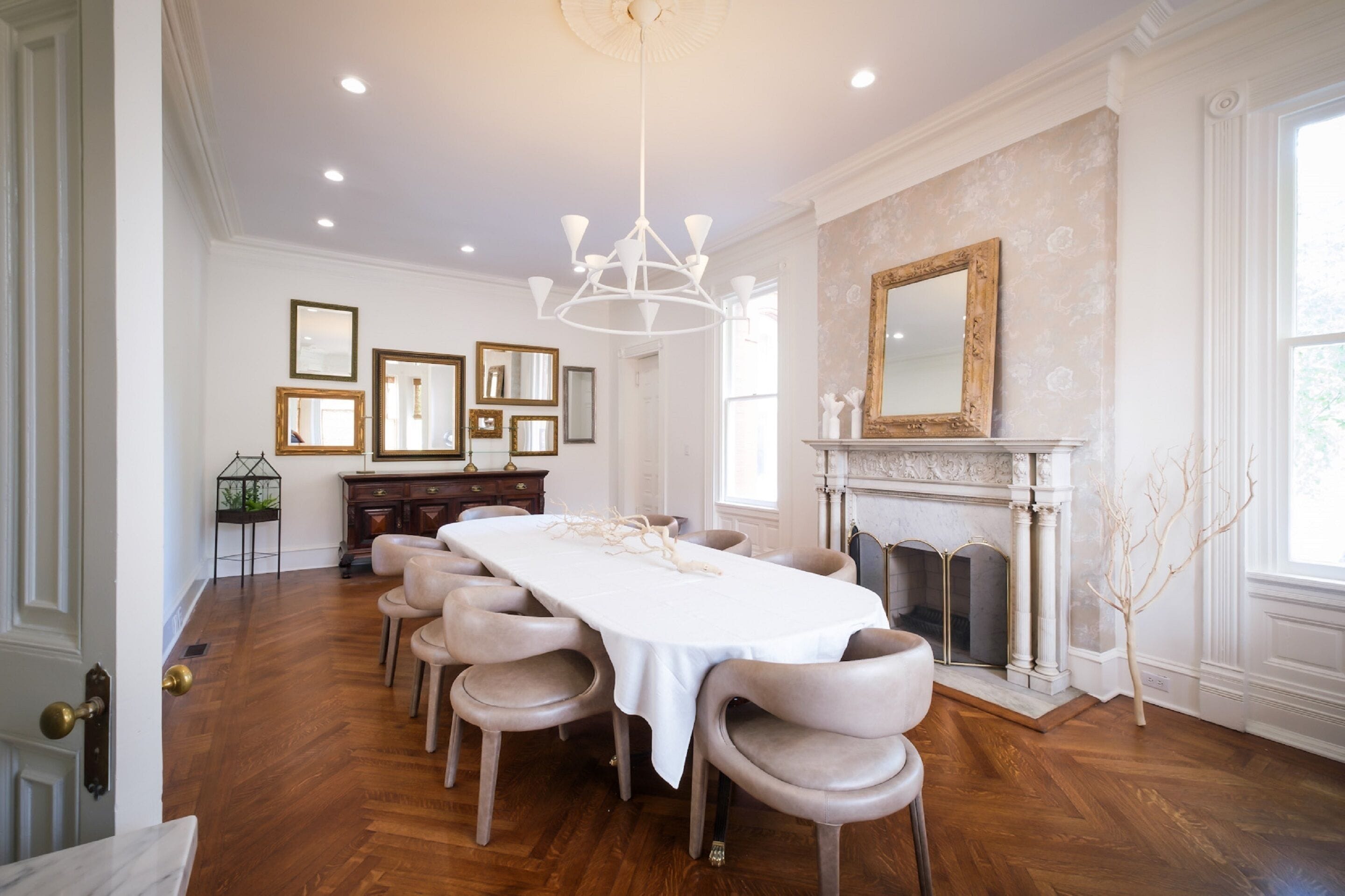 A dining room with a long table, chairs, a chandelier, framed pictures, and a fireplace.