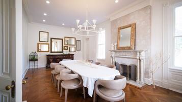 A dining room with a long table, chairs, a chandelier, framed pictures, and a fireplace.