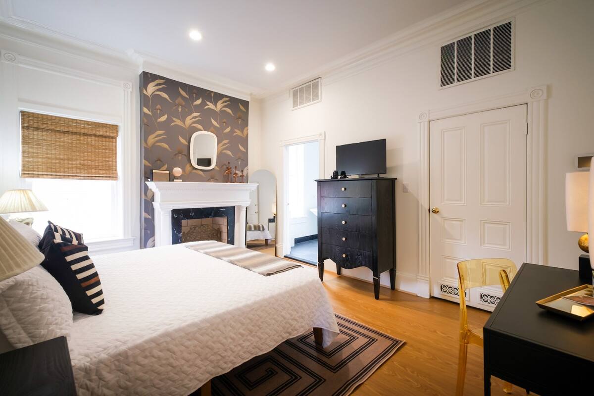 A bedroom with a large bed, a fireplace, a television, and a desk with a chair.