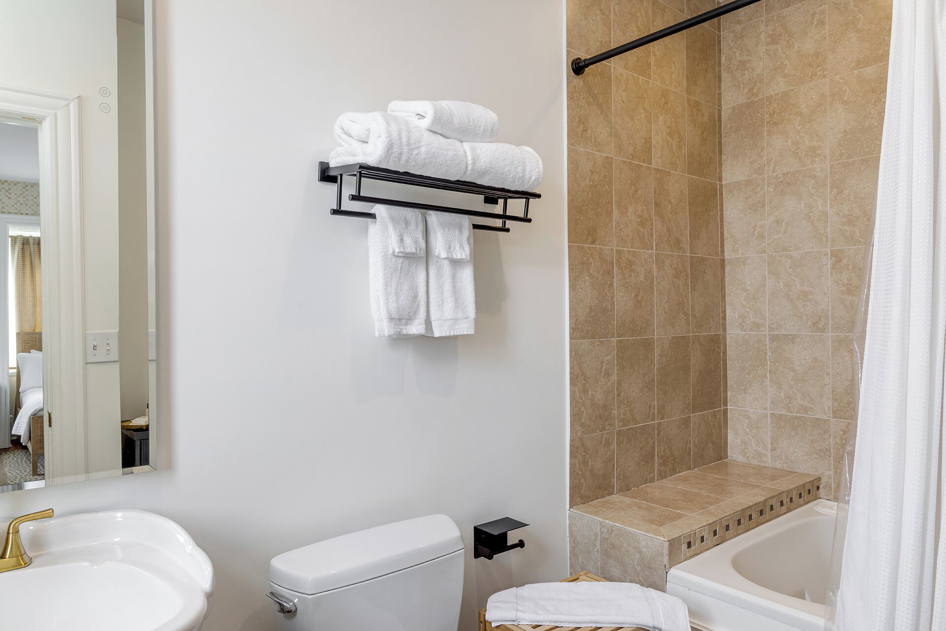 A bathroom with a white sink, toilet, and bathtub, a towel rack with towels, and beige tiled walls.