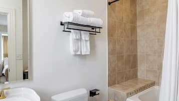 A bathroom with a white sink, toilet, and bathtub, a towel rack with towels, and beige tiled walls.