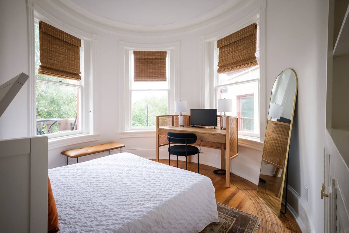 A bedroom with a bed, desk, chair, and a large mirror.