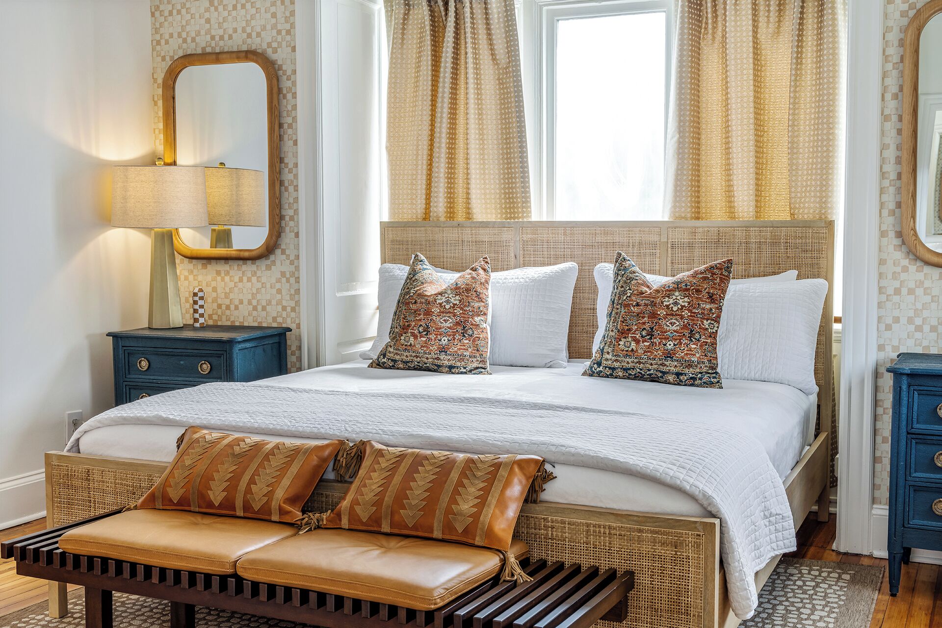 A bedroom with a large bed, a bedside table, a bench, and a mirror.