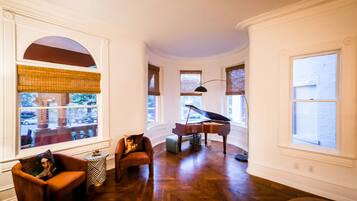 Une pièce spacieuse avec un grand piano, un parquet et de grandes fenêtres équipées de stores.