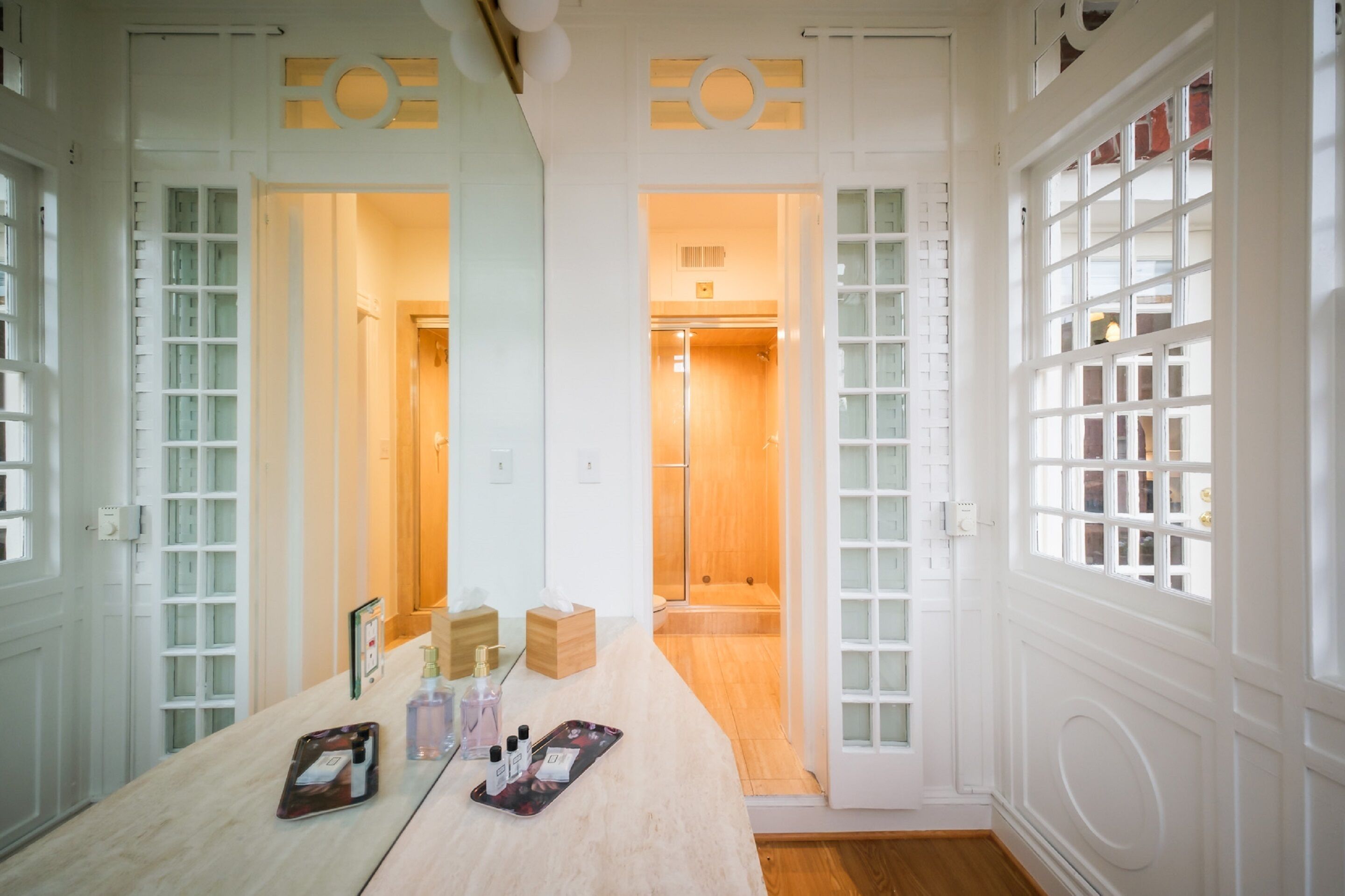 Camera d'albergo con pavimento in legno, un grande specchio, una toeletta con articoli da toilette e zona doccia.