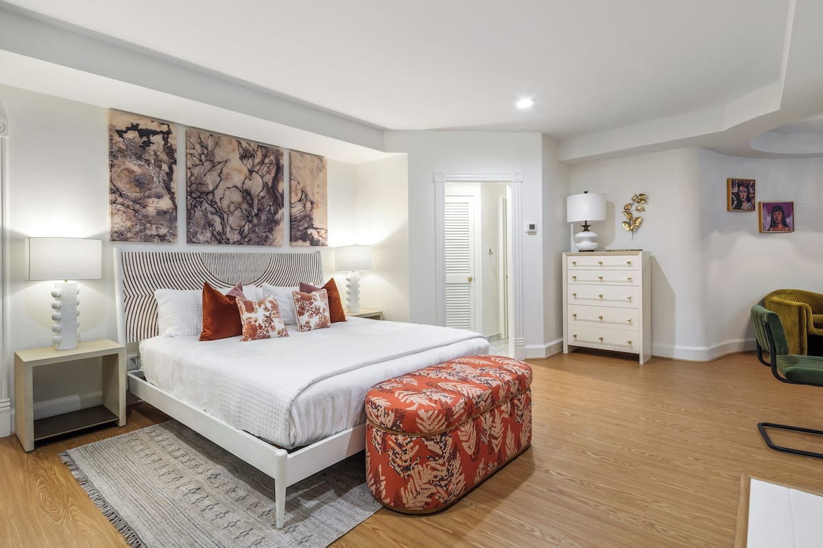 A bedroom with a large bed, a nightstand, a dresser, and a bench.