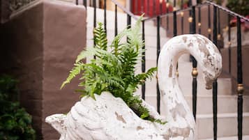 A swan-shaped planter with greenery on a pedestal in a courtyard with a staircase and red walls.