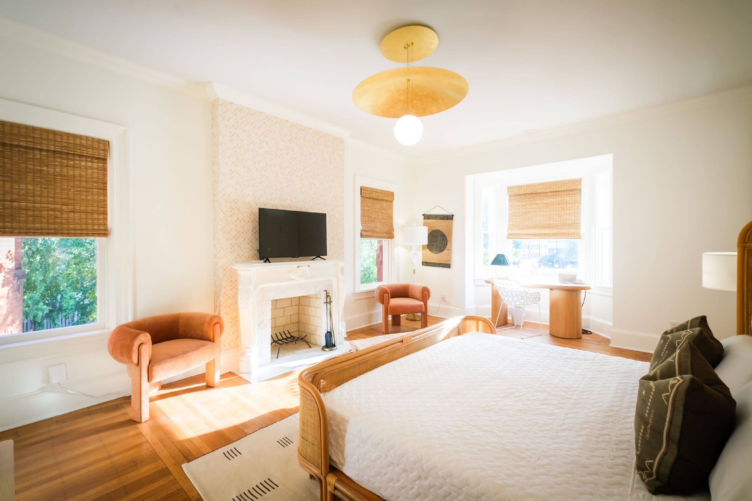 A bedroom with a large bed, a television, a fireplace, and a desk with a chair.