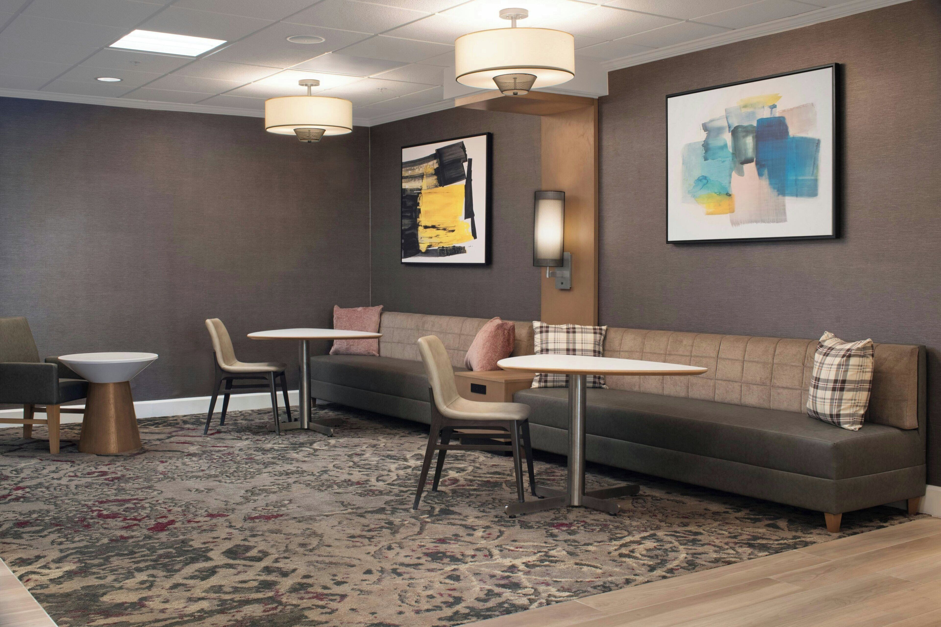 Un espace de détente moderne comprenant un canapé, des fauteuils, des tables et des œuvres d’art accrochées aux murs.