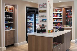 Una tienda bien organizada con estantes llenos de aperitivos, un refrigerador y un mostrador de exhibición con una máquina de café.