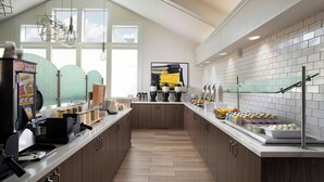 Une cuisine moderne équipée d’une machine à café, de distributeurs d’aliments et d’une vitrine en verre où sont exposés divers produits alimentaires.