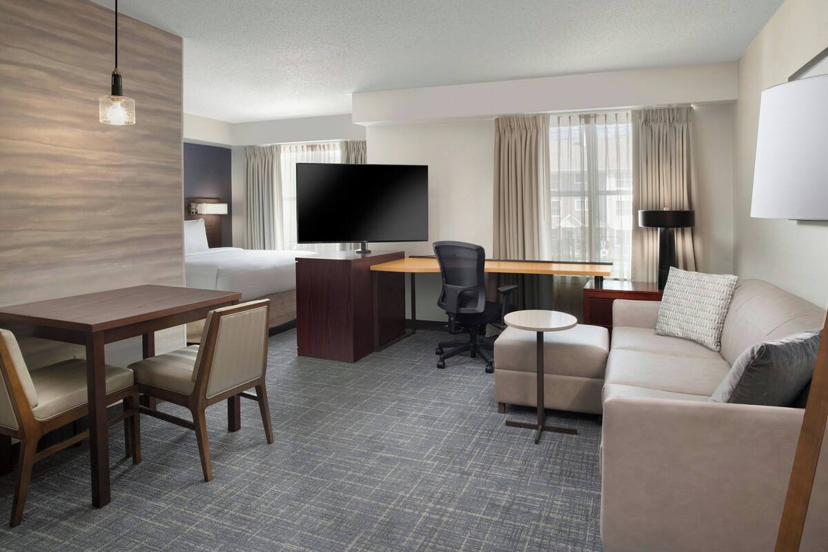 Ein Hotelzimmer mit Bett, Schreibtisch mit Stuhl, Fernseher, Sofa und Lampe.