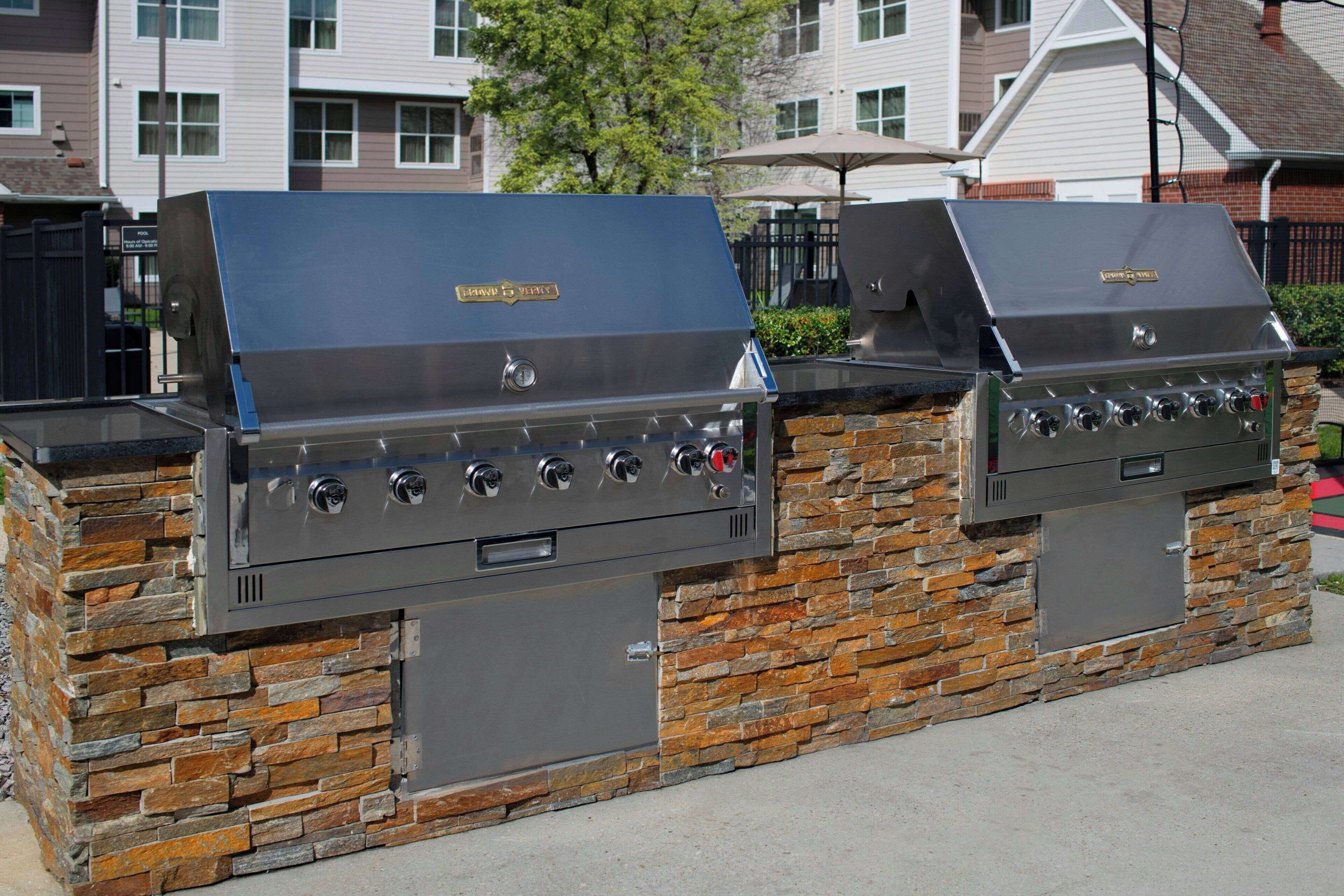 Deux barbecues à gaz d’extérieur, dotés d’une base en pierre, installés devant une maison.