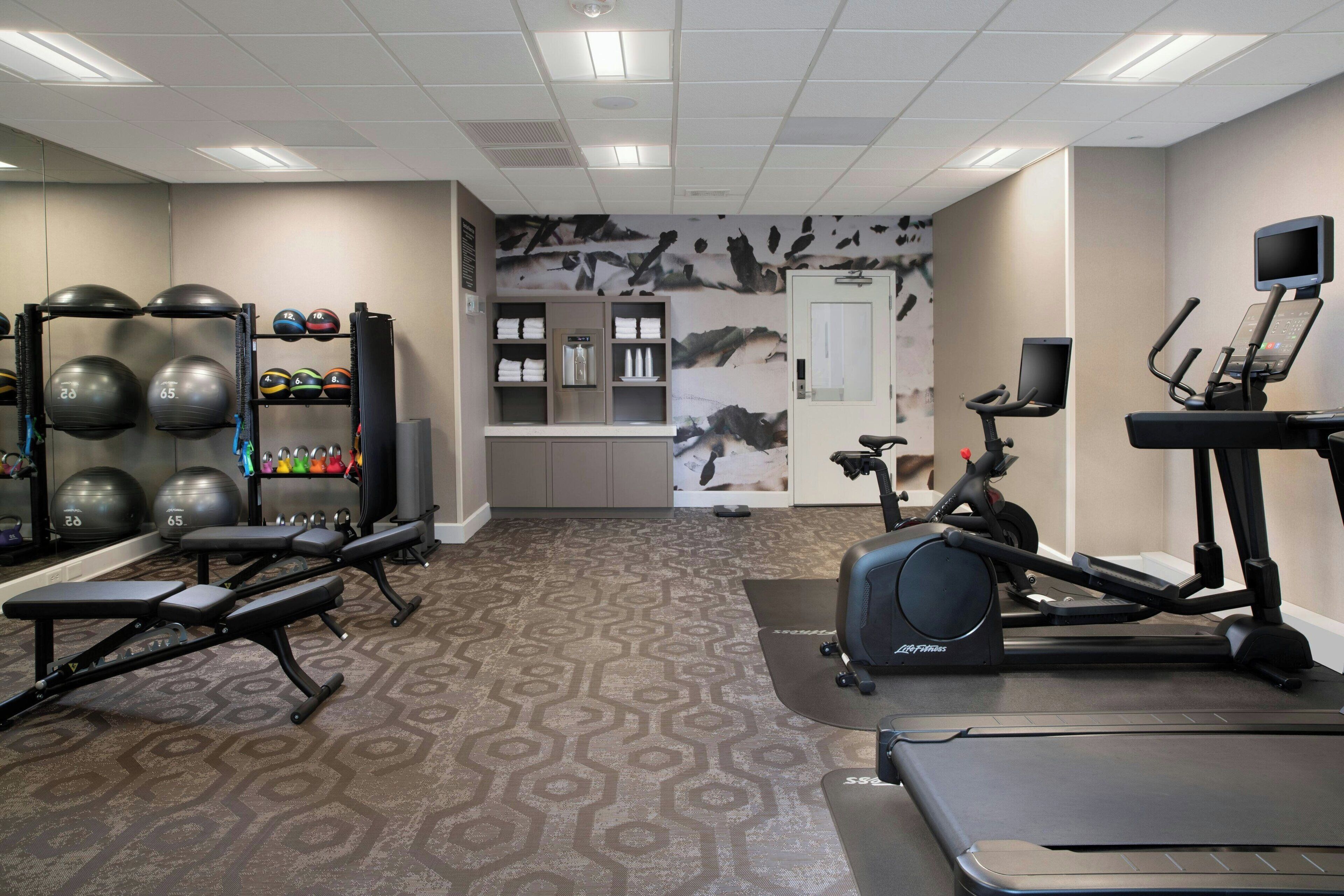 Un gimnasio con equipo de ejercicio, alfombra estampada y una pared con un mural de motivos naturales.
