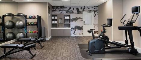 Un gimnasio con equipo de ejercicio, alfombra estampada y una pared con un mural de motivos naturales.