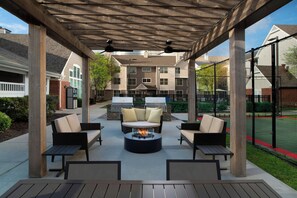 Een terras buiten met een vuurkuil, zitplaatsen en een barbecue.