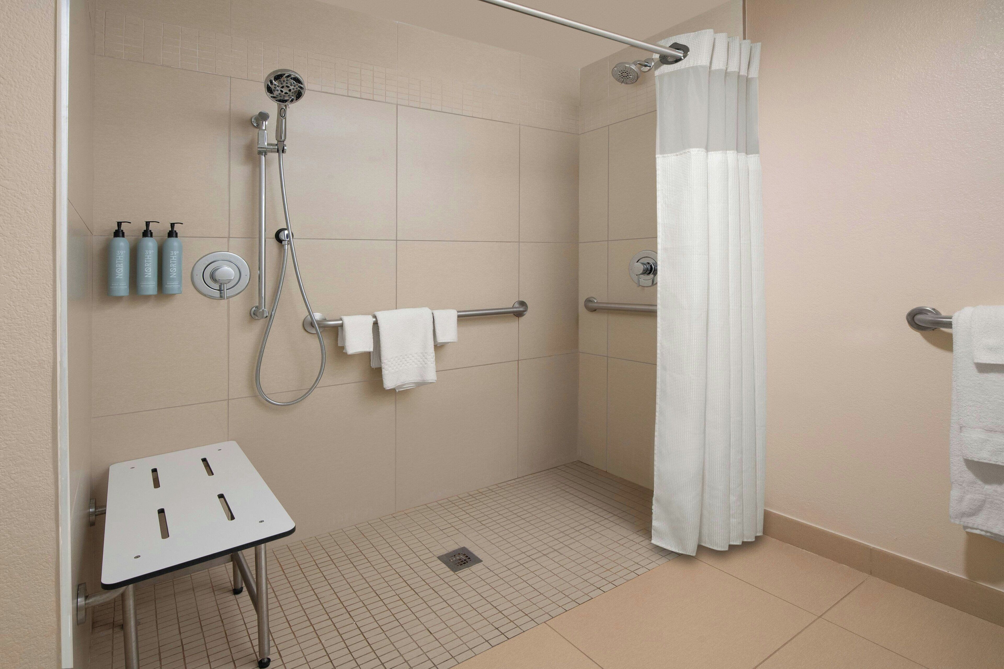 A modern bathroom with a shower, a toilet, and a sink. There are towels and toiletries on the wall.