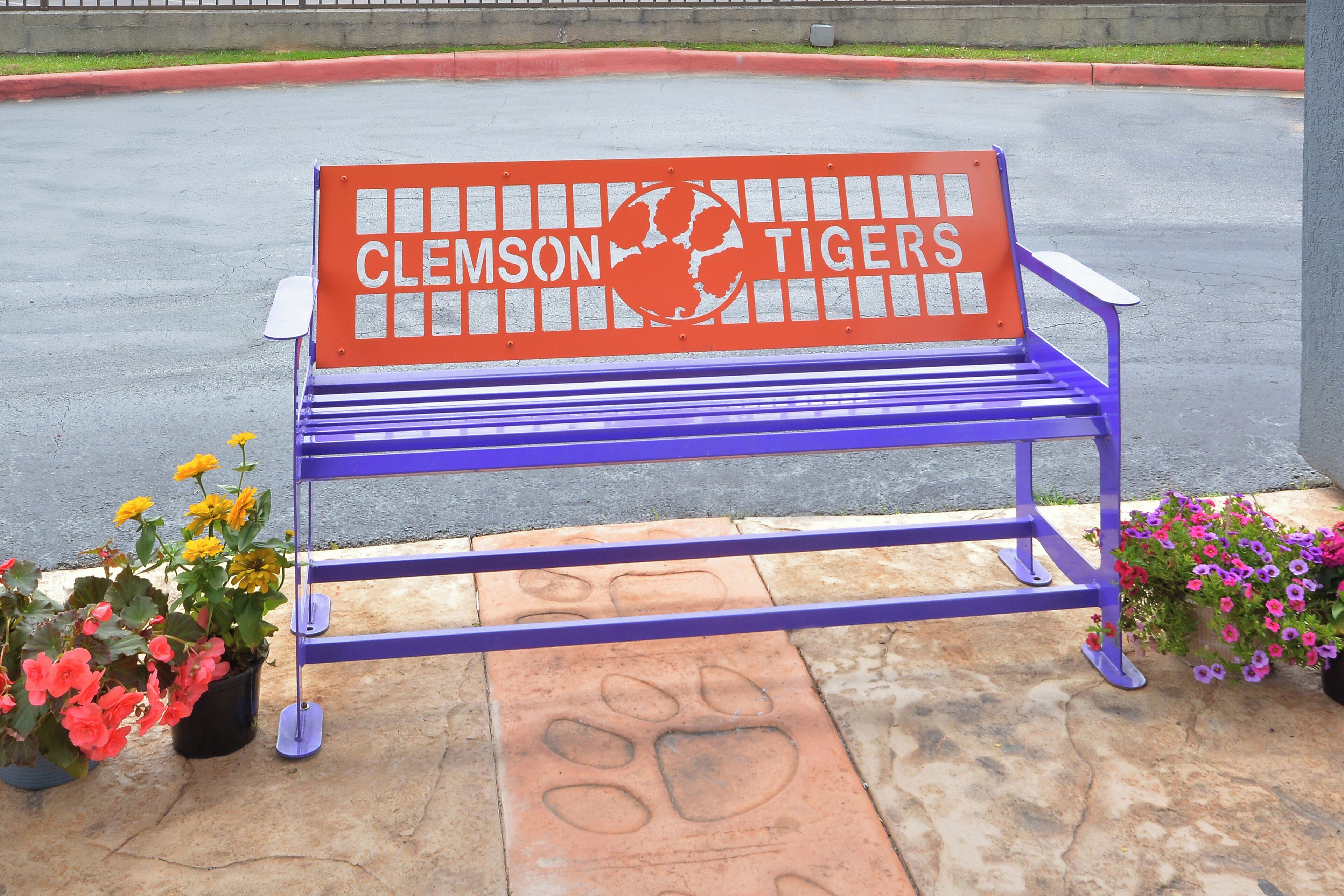 A purple bench with "Clemson Tigers" written on it, surrounded by potted plants.