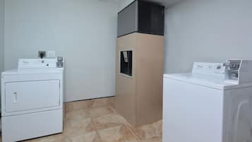 A laundry room with two stacked washers and a dryer, a vent hood, and a control panel.