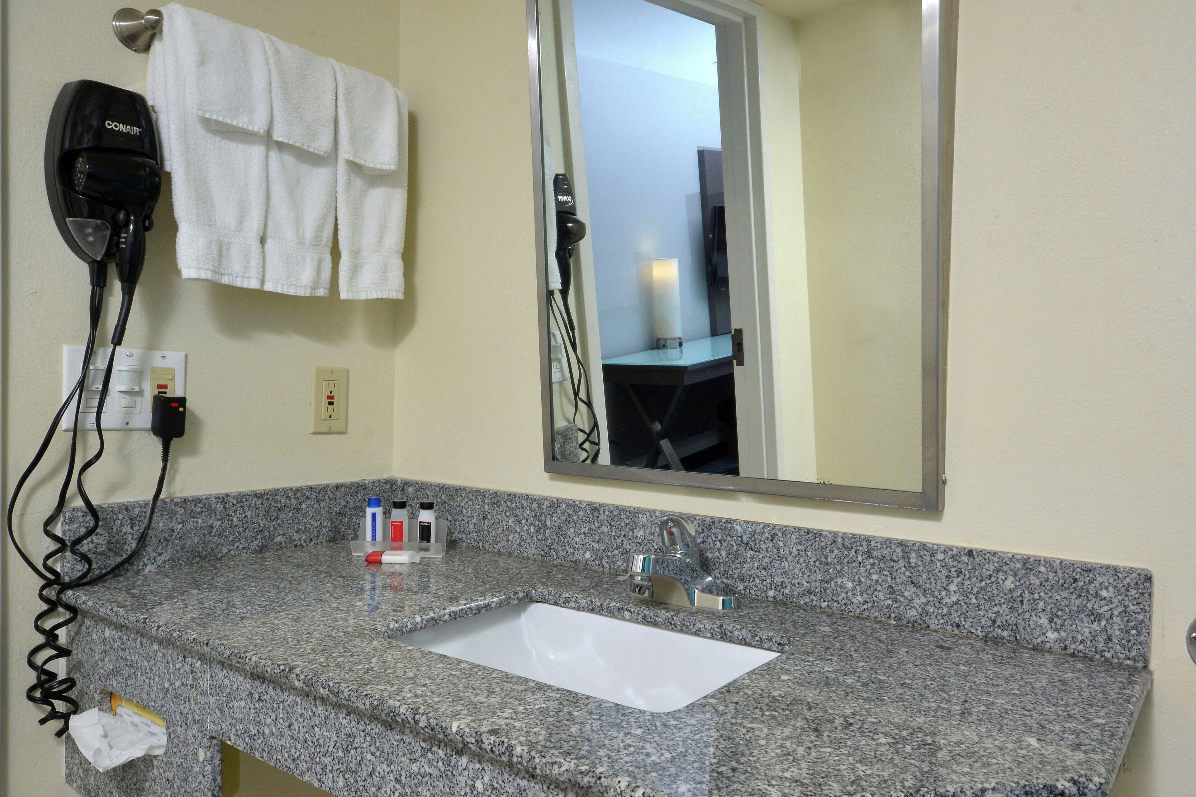 A bathroom with a granite countertop, a white sink, a hairdryer, and a mirror.