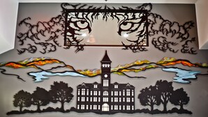 Un mur orné d’un motif décoratif représentant un bâtiment, des arbres et un ciel nuageux.