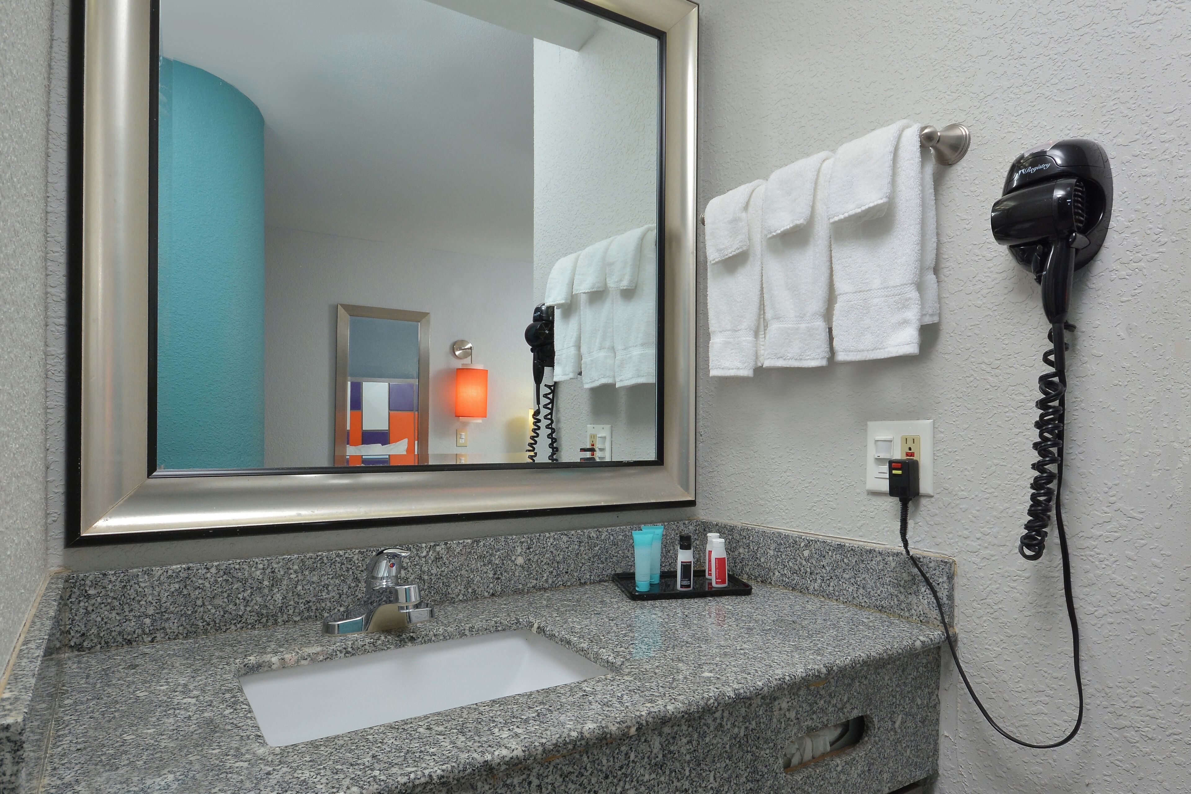 A bathroom with a granite countertop, a sink, a mirror, a hairdryer, and a towel rack.