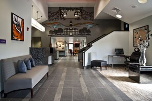 Zona de recepción con mostrador, sofá, escalera y una pared decorada con obras de arte.