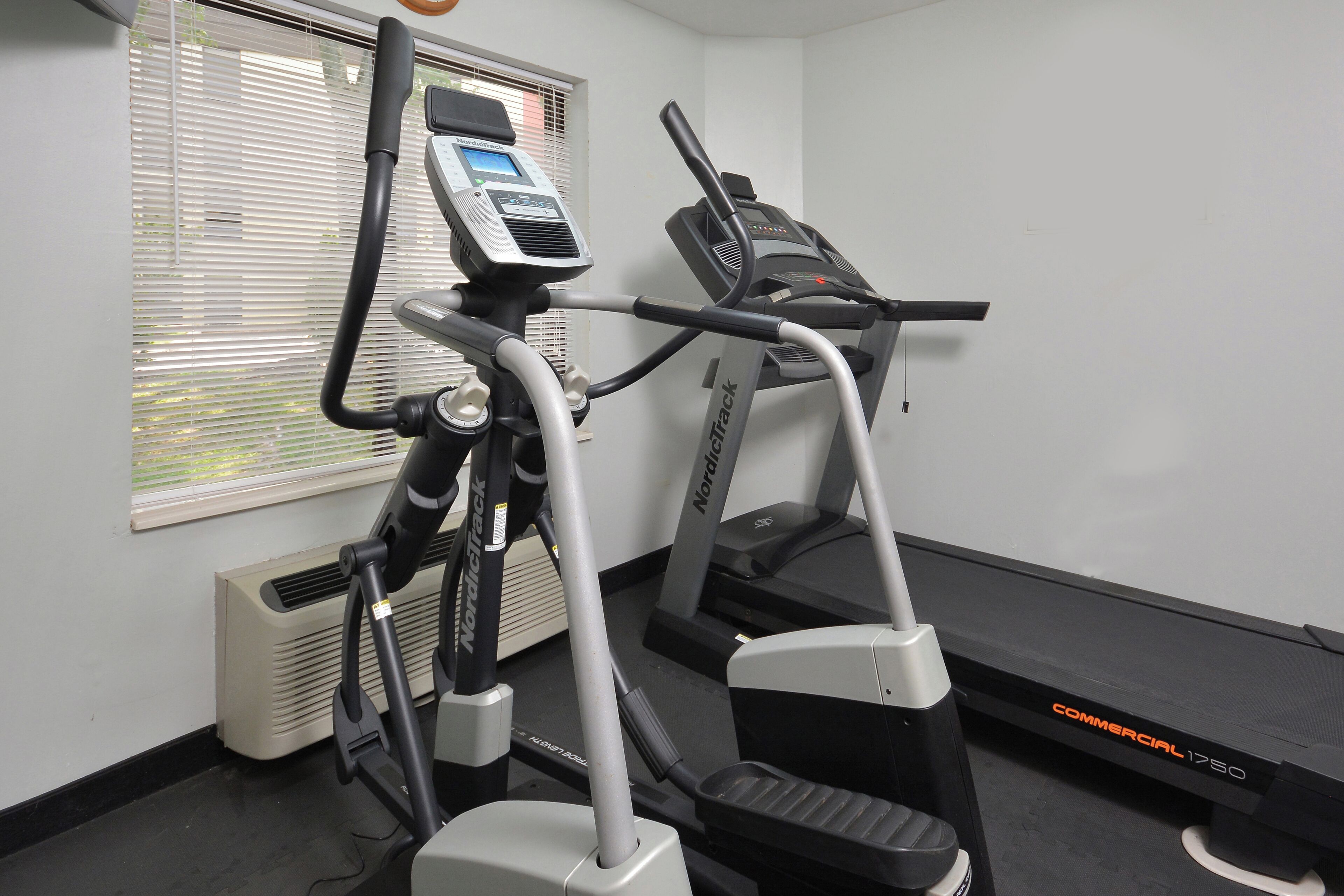 Een sportschool met cardioapparaten, waaronder een loopband en een crosstrainer, plus een bankje.