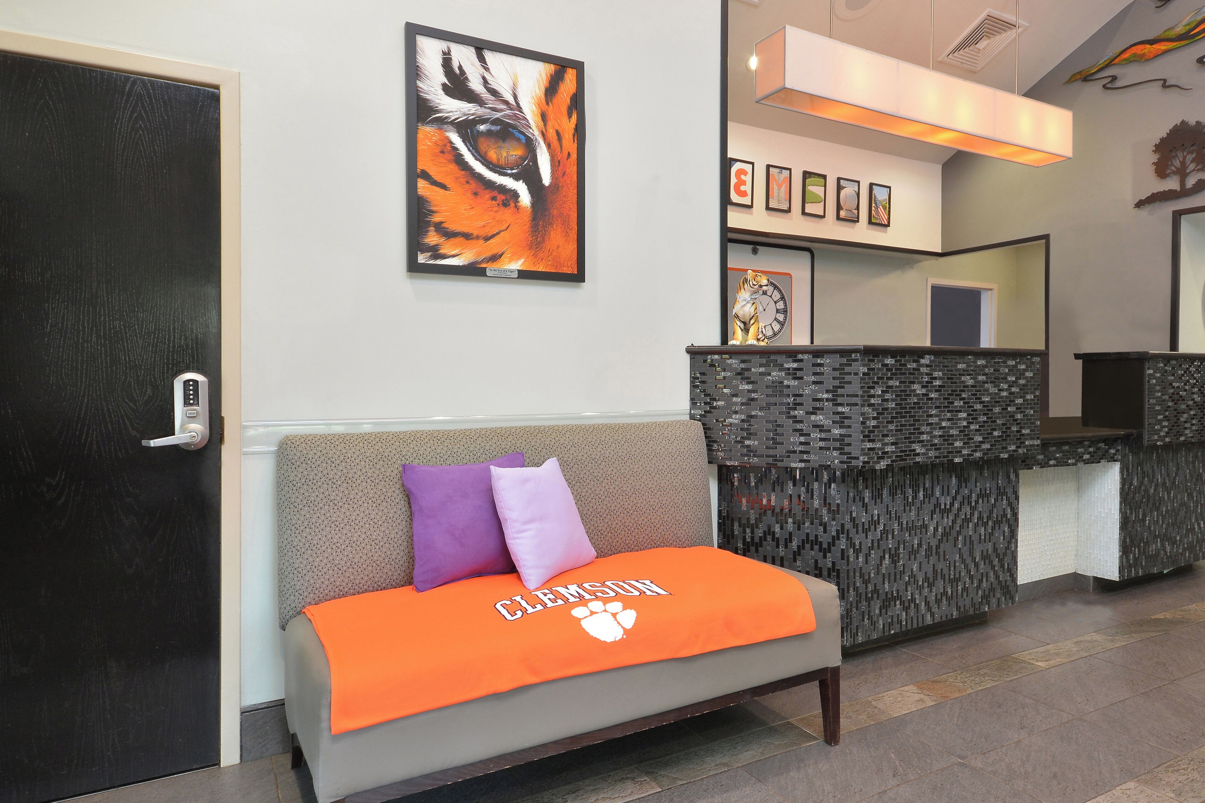 Un espace d’accueil comprenant un canapé, une couverture aux couleurs de Clemson, une œuvre d’art représentant un tigre, un comptoir d’accueil et une horloge.