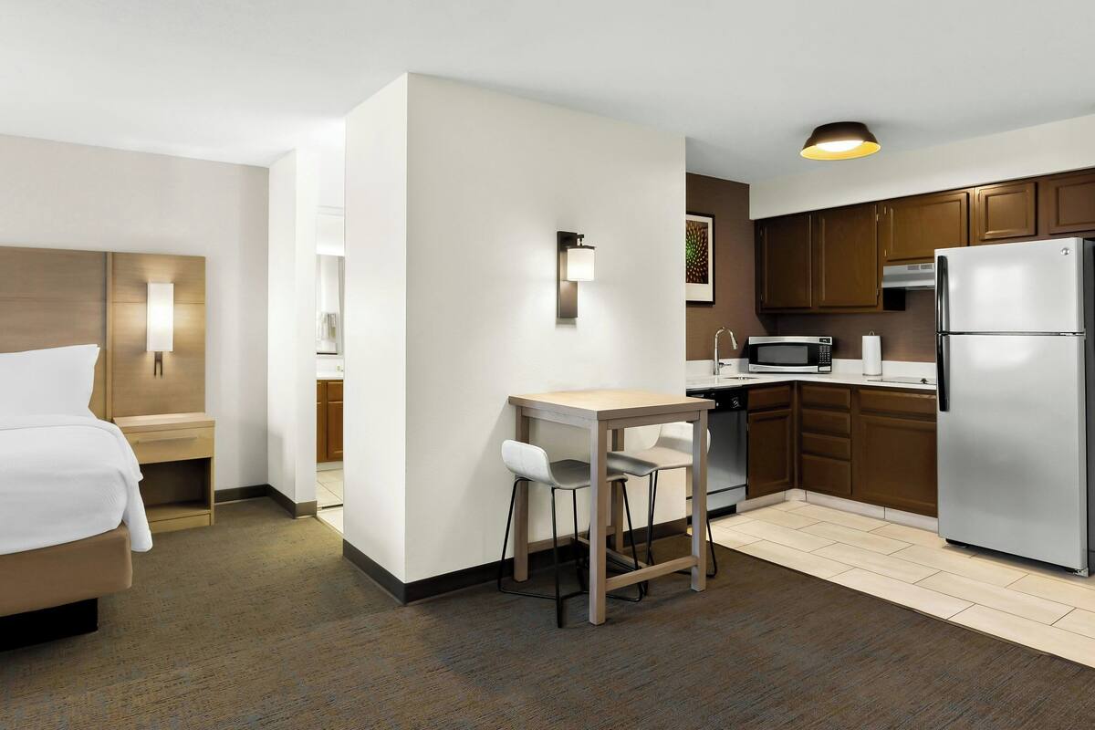 A hotel room with a bed, a small table with two chairs, a microwave, a refrigerator, and a sink.