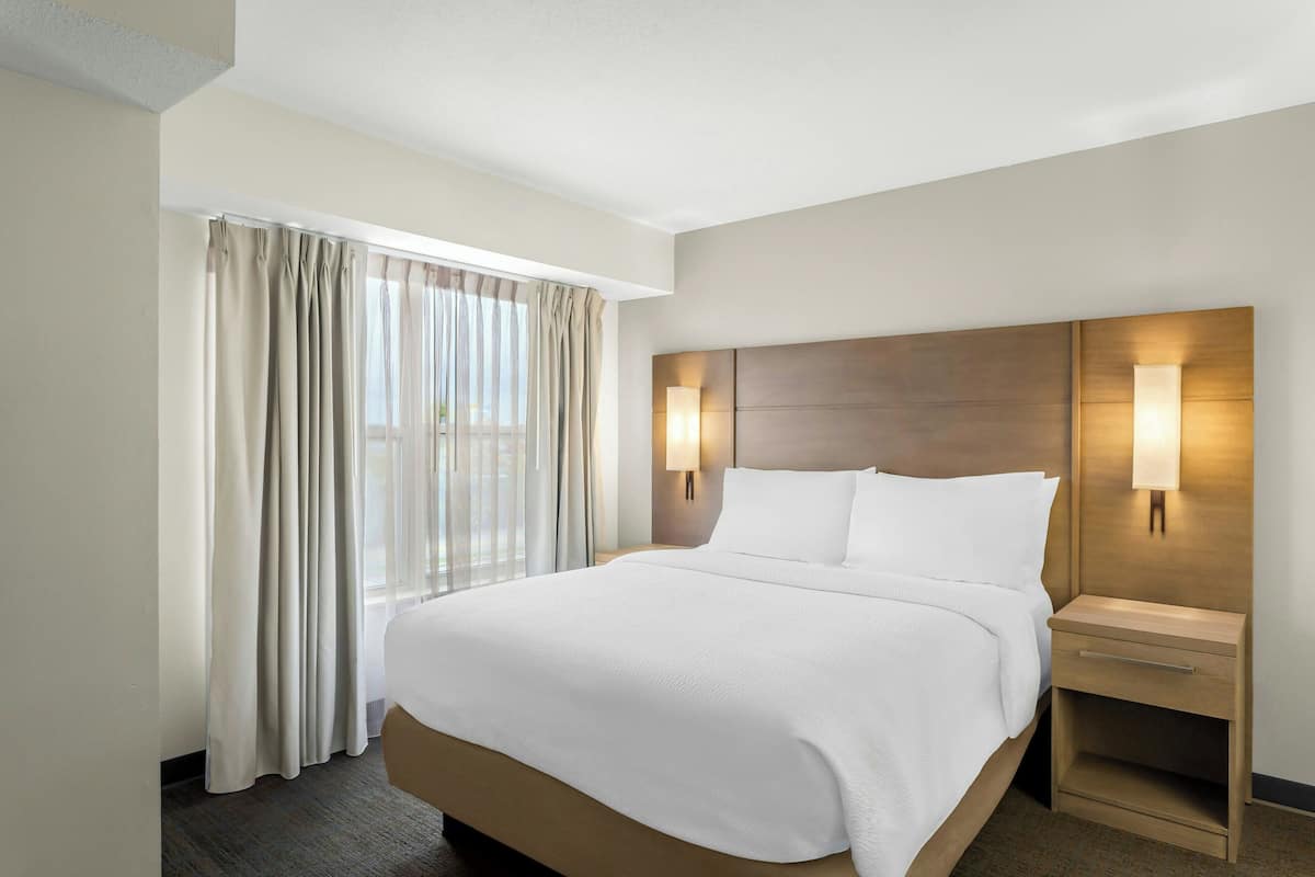 A hotel room with a large bed, two bedside tables, a nightstand, and a window with curtains.