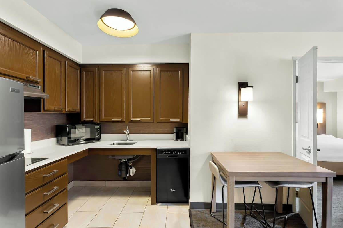 A compact kitchen with wooden cabinets, a built-in microwave, a dishwasher, and a small dining area with a table and chairs.