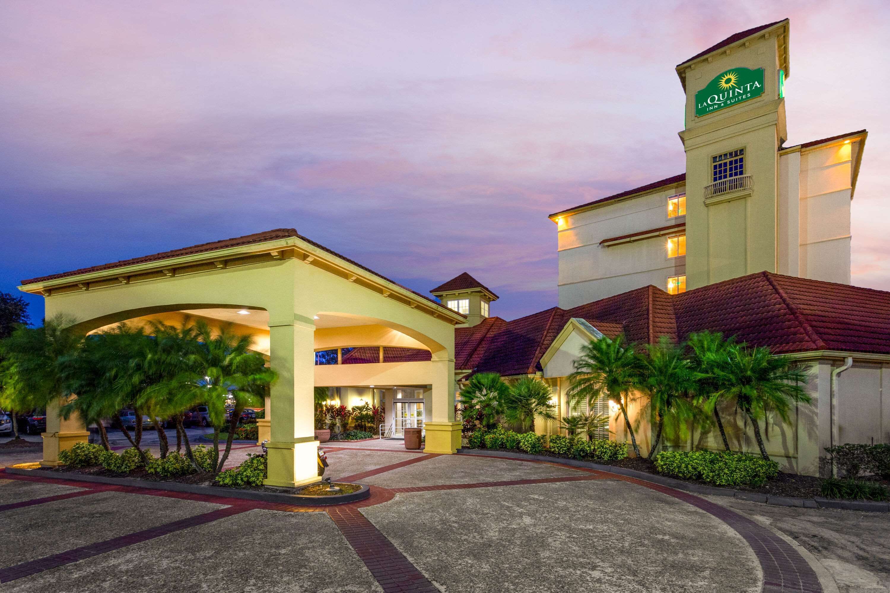 A hotel entrance with a covered walkway, palm trees, and a sign indicating it's a La Quinta Inn & Suites.