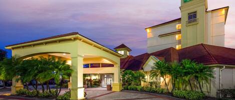 A hotel entrance with a covered walkway, palm trees, and a sign indicating it's a La Quinta Inn & Suites.