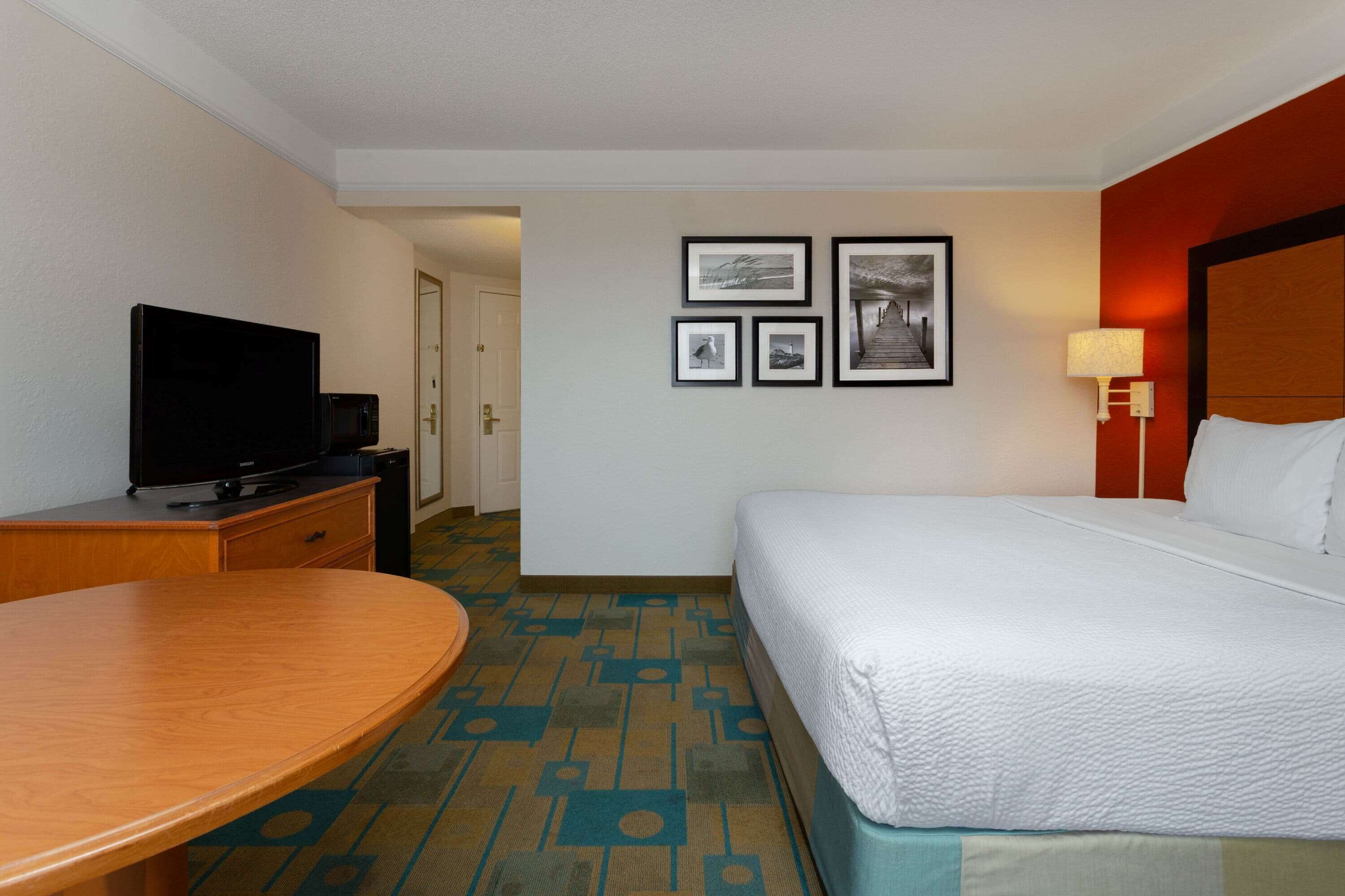 A hotel room with a bed, a desk, a television, and a door leading to another room.