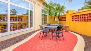 An outdoor patio with a round table and chairs, surrounded by a red brick floor and yellow walls.