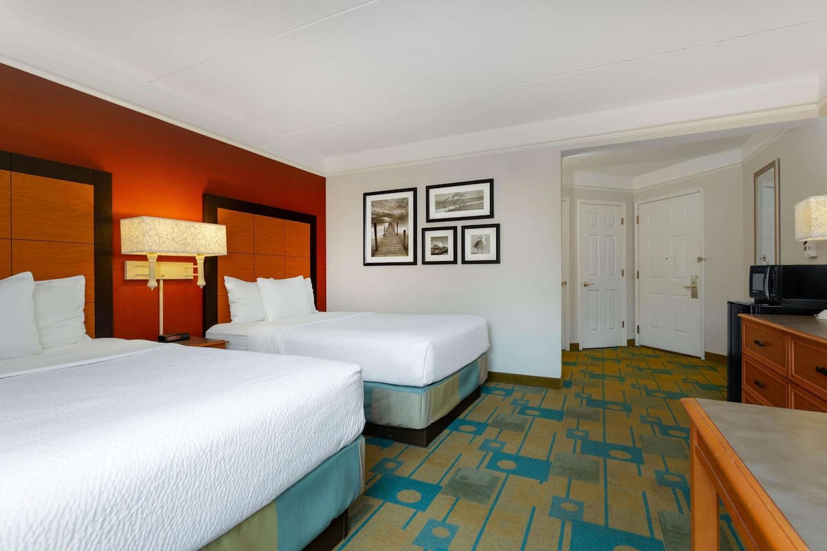 A hotel room with two beds, a desk, a lamp, and a television.