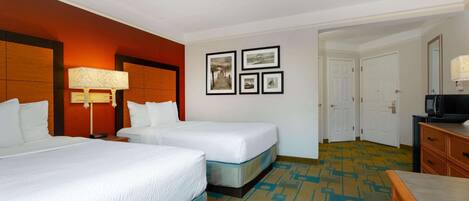 A hotel room with two beds, a desk, a lamp, and a television.
