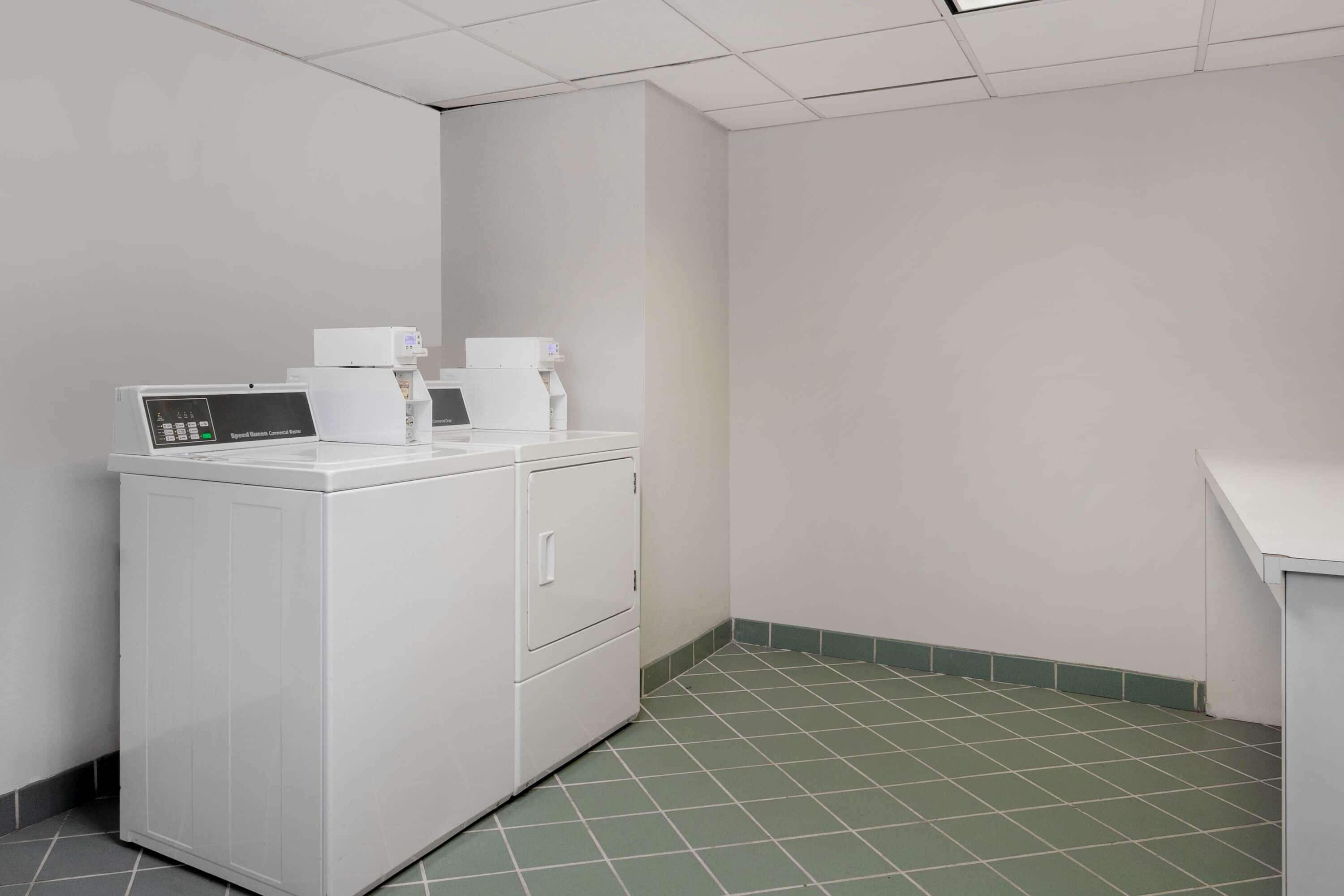 A laundry room with a front-loading washer and dryer, green-tiled floor, and white walls.