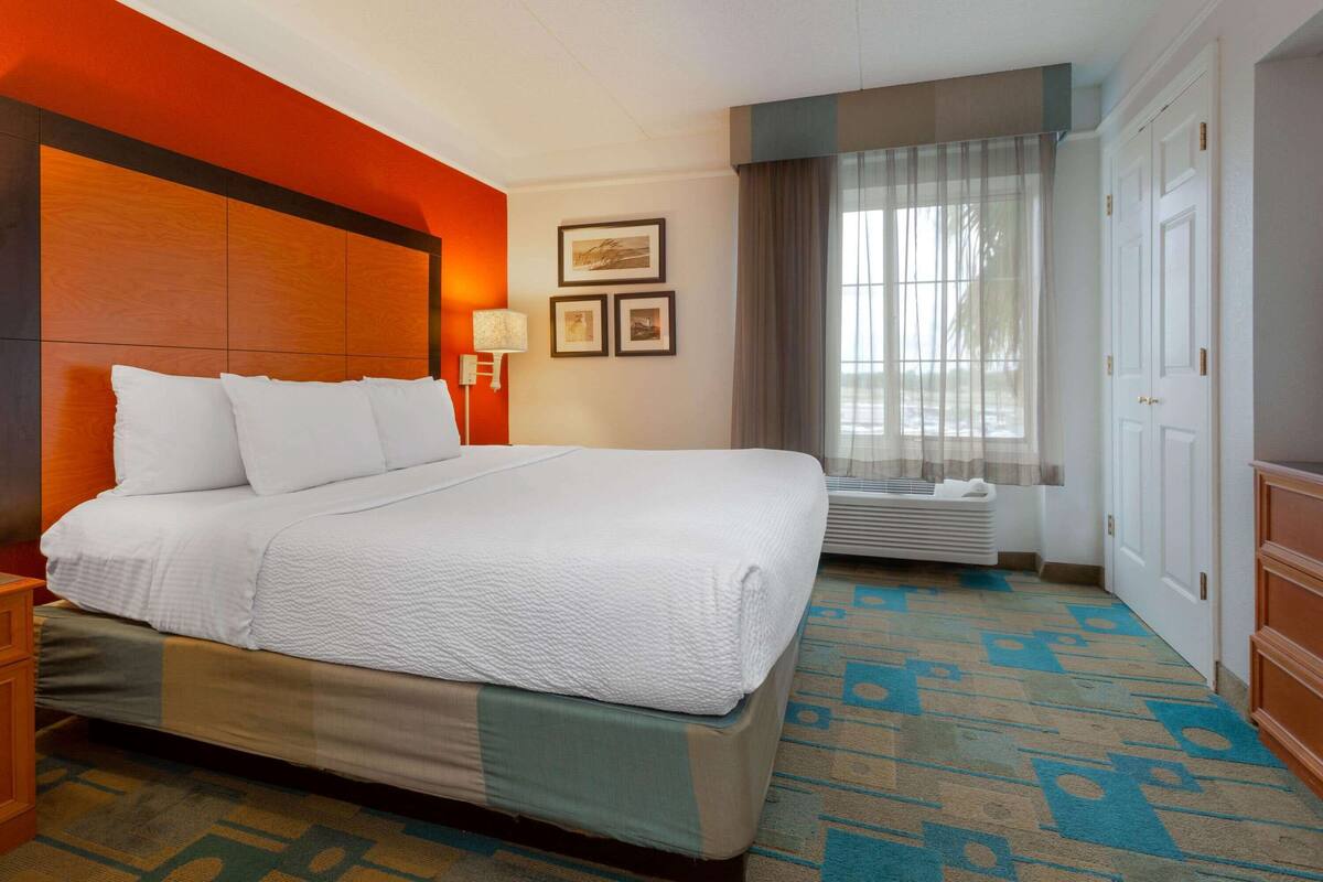 A hotel room with a large bed, a nightstand, a lamp, a window with curtains, and a door.