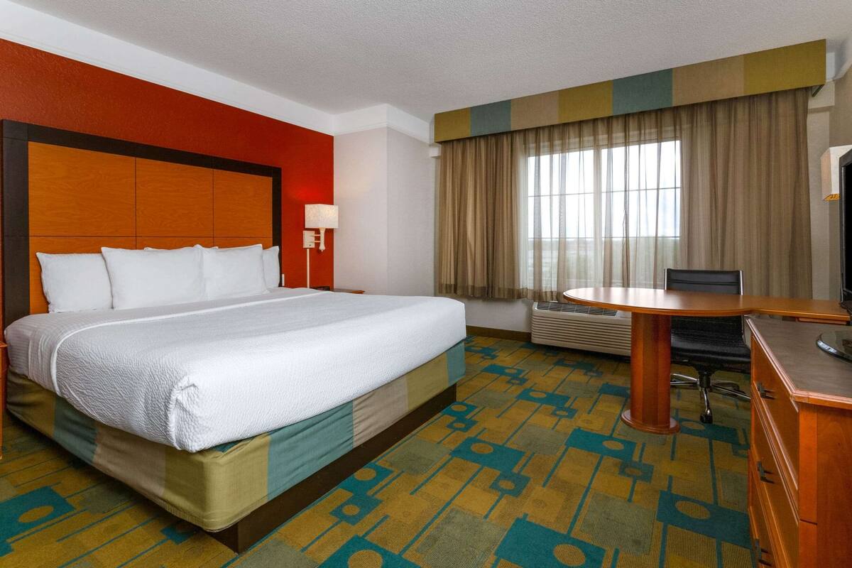 A hotel room with a large bed, a desk with a chair, a lamp, and a window with curtains.