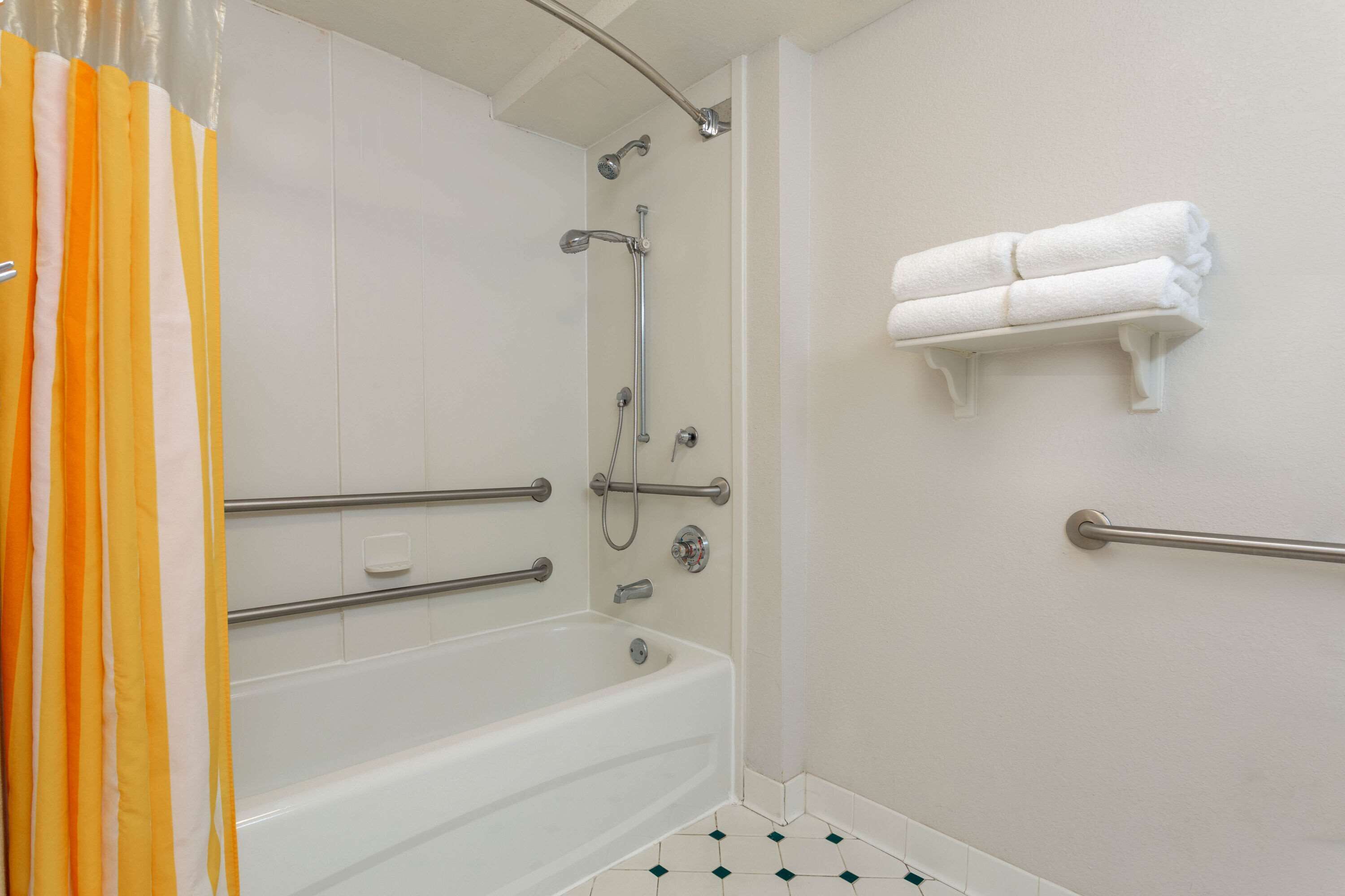 A bathroom with a bathtub, shower, and handrails.