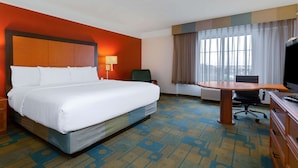 A hotel room with a large bed, a desk, a chair, a television, and a window with curtains.