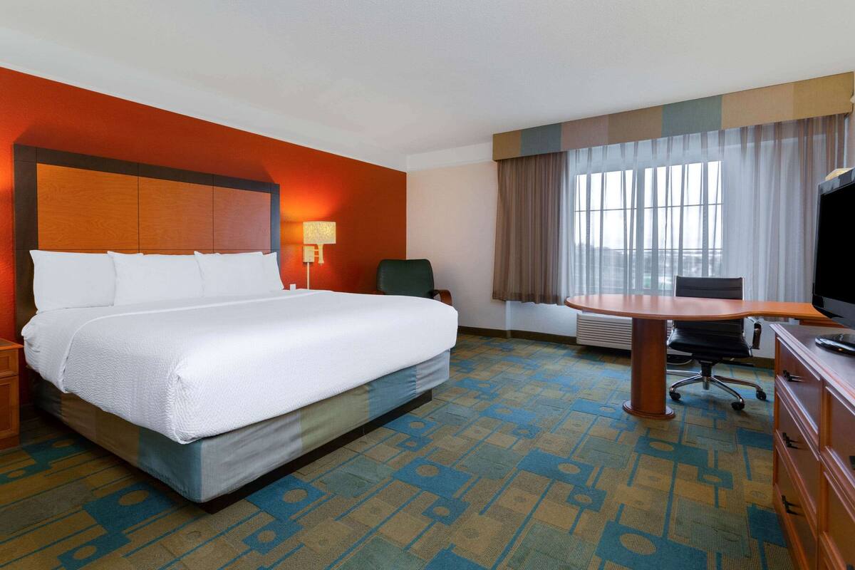 A hotel room with a large bed, a desk, a chair, a television, and a window with curtains.