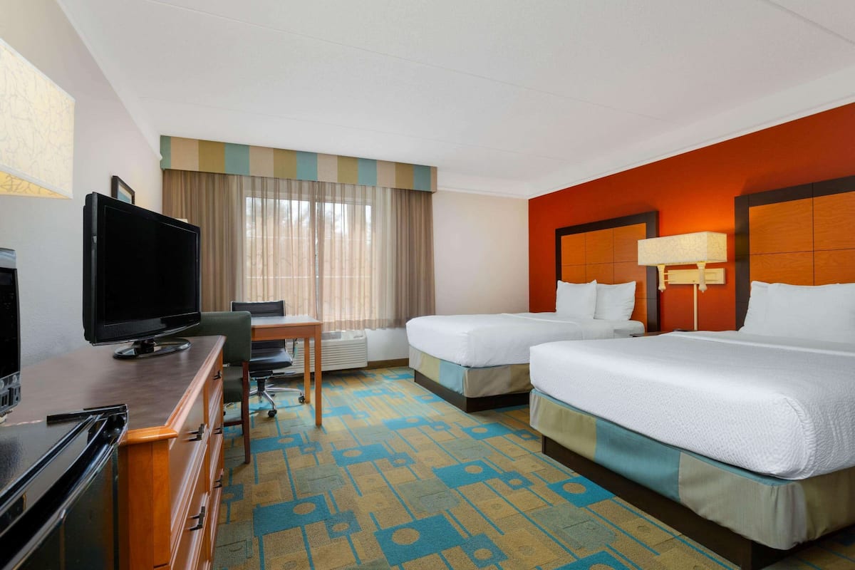 A hotel room with two beds, a desk with a TV, and a patterned carpet.