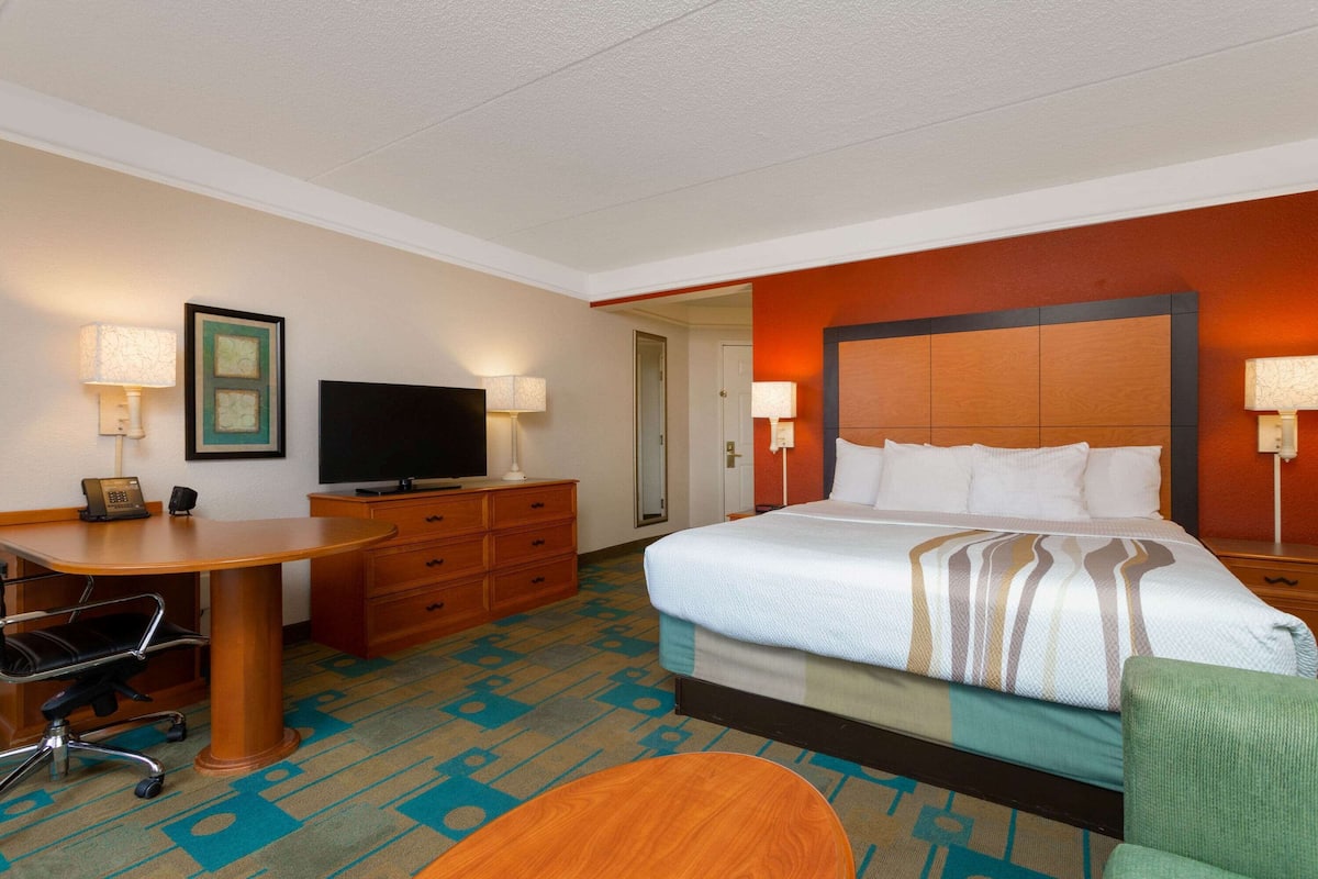 A hotel room with a bed, desk, chair, television, and a door leading to another room.