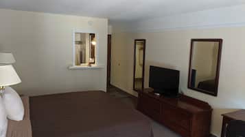 A hotel room with a large bed, a TV on a wooden dresser, a mirror, and a lamp.