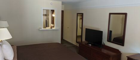Une chambre d’hôtel avec un grand lit, un téléviseur posé sur une commode en bois, un miroir et une lampe.