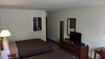 A hotel room with two beds, a desk with a television, a dresser, and a lamp.